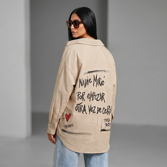 Camisa oversize oliva de rayas finas pintada a mano con la frase "Nadie murió por empezar otra vez de cero", diseño exclusivo de Paola Santos.