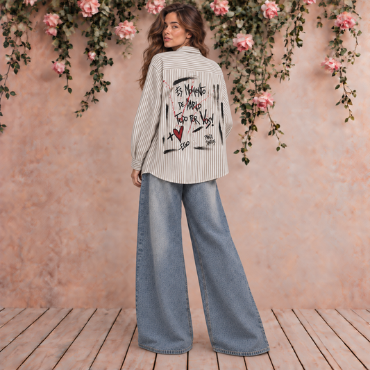 Camisa rayada beige y blanca de corte amplio con intervención artística y frase Es momento de darlo todo por vos en la espalda, diseño Paola Santos.