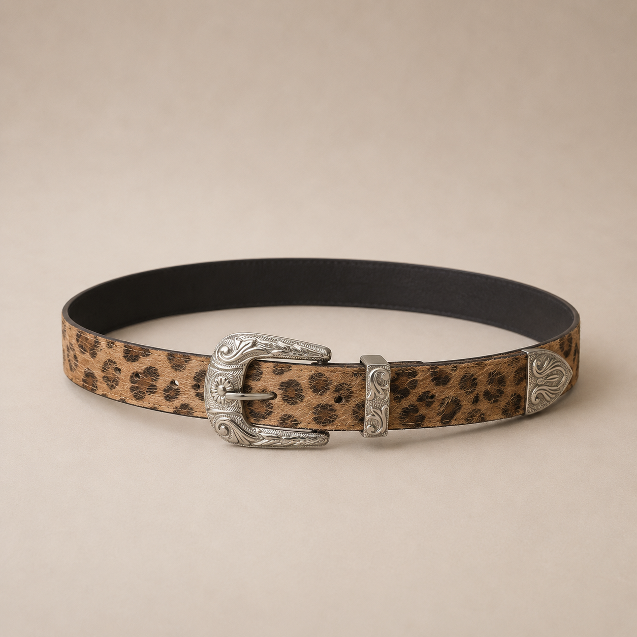 Cinto fino animal print en tonos camel y negro con hebilla metálica plateada estilo western y detalles grabados.