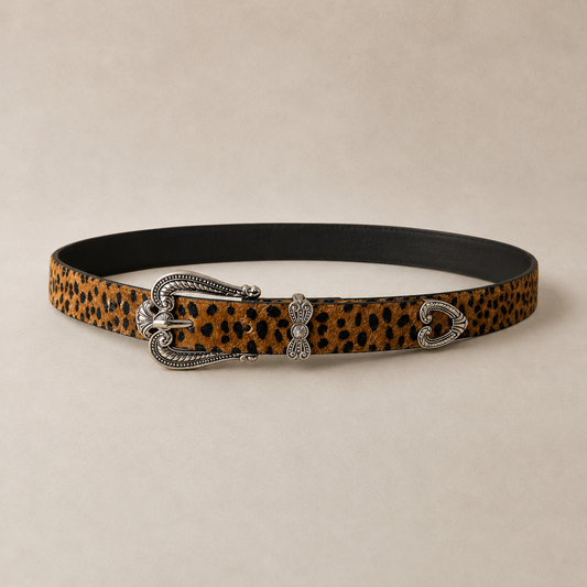 Cinto animal print en tonos camel y negro con hebilla metálica plateada estilo western y detalles ornamentales.